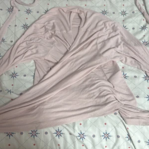 Ljusrosa omlottopp - Säljer en ljusrosa omlottopp med långa ärmar. Toppen har en mjuk och bekväm passform, perfekt för en stilren look. Den är tillverkad i ett lätt och luftigt material som gör den skön att bära.