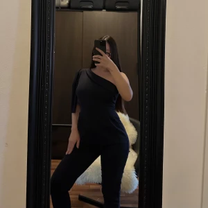 Jumpsuit - Snygg svart oneshoulder jumpsuit med en elegant passform. Perfekt för en stilren look med en ärm och en axel bar. Materialet ser ut att vara mjukt och stretchigt för en bekväm känsla.🥰🥰🥰