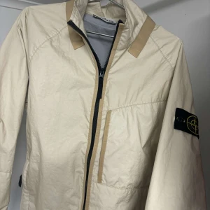 Beige jacka från Stone Island - Stilren beige vårjacka från Stone Island med dragkedja. 
