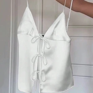 Vit satinlinne med snörning - Elegant vit satinlinne med smala axelband och rosetter framtill. Perfekt sommar topp som går att klä upp fint🤍