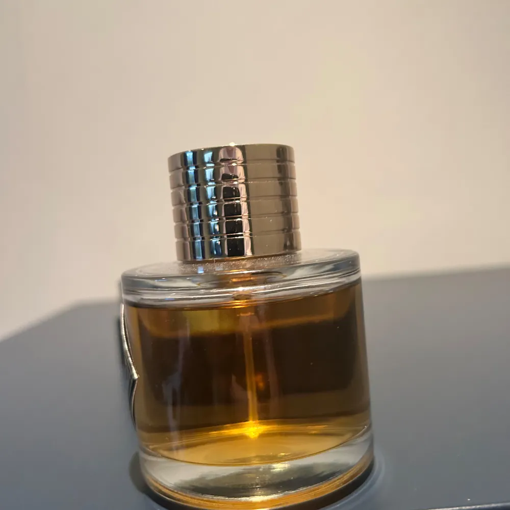 Elegant parfymflaska från Kismet Magic med en stilren design. Flaskan är rund med en gyllene vätska och har en silverfärgad, räfflad kork. Etiketten är svart med vit text och ger en lyxig känsla. Perfekt för den som söker en sofistikerad doftupplevelse. Ändast testad, 99 ml kvar😁Lovar att komplimanger kommer att fås! Kvitto samt allt fås med. Perfume.