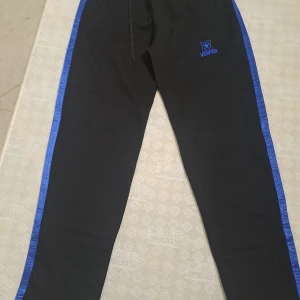 Svarta mjukisbyxor med blå detaljer från Vesper - Snygga svarta mjukisbyxor från Vesper med blå ränder längs sidorna. Byxorna har en elastisk midja med snörning för justerbar passform. Perfekta för en avslappnad stil.