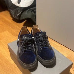 Blå giuseppe zanooti skor med dragkedja - Snygga blå sneakers i sammet från Giuseppe Zanotti med svarta snören och dragkedja på sidan. Skorna har en robust svart sula och en stilren design som passar perfekt för en trendig look.