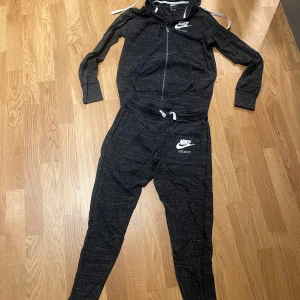 Svart mjukisbyxa XS och jacka S från Nike - Säljer ett par svarta mjukisbyxor XS från Nike med det klassiska 'Just Do It'-trycket. Byxorna har en bekväm passform och är perfekta för en avslappnad stil. De har en dragsko i midjan för justerbar passform. Kommer med jackan i storlek S