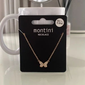 Guldhalsband med fjäril från Ur&penn  - Elegant guldhalsband från Montini med en glittrig fjärilsberlock. Perfekt för att lägga till en touch av glamour till din outfit. Kedjan är tunn och smidig, vilket gör den bekväm att bära hela dagen.