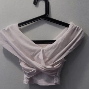 Ljusrosa offshoulder topp - Säljer en vit offshoulder topp med omlott-design. Toppen är croppad och har en elegant drapering framtill. Perfekt för en stilren look