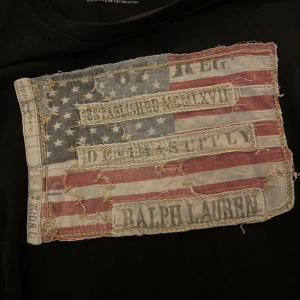 Svart t-shirt från Ralph Lauren - Säljer en svart t-shirt från Ralph Lauren med en stor, sliten amerikansk flagga på bröstet. T-shirten är tillverkad i 100% bomull och kommer från kollektionen Denim & Supply. Priset kan diskuteras 
