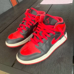 Air Jordan 1 mid - Banned - Snygga Nike Air Jordan 1 i svart och rött med klassisk design. Dessa skor är mellan låga och höga Air jordans, alltså modellen mid. Skorna är en snygg modell med röd snörning och en vit sula som kontrasterar mot det svarta och röda lädret. Perfekta för dig som vill ha en ett par feta skor. Riktigt feta Air Jordans i storlek 39 och passar både killar och tjejer. Modellen heter ”Banned” och är en väldigt unik och snygg modell. Skick 8/10, Priset går att diskuteras i pm!