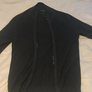 Svart kofta från Andrew James - Snygg svart kofta från Andrew James i ekologisk bomull. Perfekt för en stilren look med sin enkla design och bekväma passform. Ett måste i garderoben för alla tillfällen.