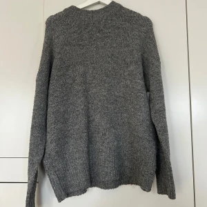 Grå stickad tröja från 157 - Säljer en mysig grå stickad tröja från 157. Perfekt för kyliga dagar med sin mjuka och bekväma passform. Tröjan har långa ärmar och en klassisk rund halsringning. Ett måste i garderoben för en stilren look. Oversized i modellen skulle jag säga 