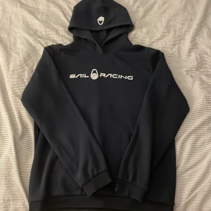 Svart hoodie från Sail Racing - Säljer en snygg och bekväm svart hoodie från Sail Racing. Den har en klassisk design med logga på bröstet och huvan. Perfekt för både vardag och chill. Hör av dig om du är intresserad!
