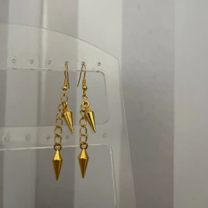Guldiga örhängen med kedja och spetsiga hängen - Snygga och trendiga guldiga örhängen med en kedja och spetsiga hängen. Perfekta för att ge en edgy touch till din outfit. De är lätta och bekväma att bära hela dagen. Passar både till vardags och fest!