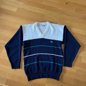Vintage Lacoste V-neck Sweater - Vinatage Lacoste V-Neck Sweater. Egentliga syftet är en tröja för primärt tennis, men även lämpad för golf eller till vardags. Lite nopprig av åldern. Tidigare ägare har tagit bort tvättlappen, vilket kan ses då sömmen är kvar. 