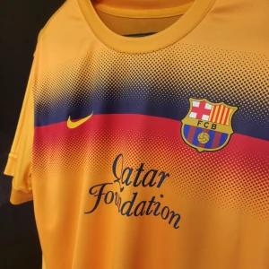 FC Barcelona Tränings Tröja - Säljer en FC Barcelona fotbollströja från Nike i Dri-FIT material. Tröjan har ett coolt mönster med blå och röda detaljer över bröstet. På framsidan finns Qatar Foundation-loggan och klubbmärket, medan baksidan har texten 'BARÇA'. 100% Authentic 