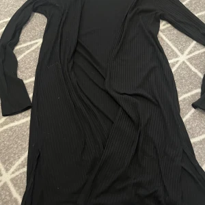 Svart kofta - Säljer en svart ribbad kofta från Lindex i storlek EUR 170. Koftan har långa ärmar och är perfekt för både vardag och fest. Den är i bra skick och redo för en ny ägare! Helt oanvänd. Säljer för att den är för liten.