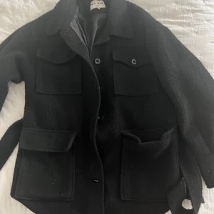 Höstkappa - Fin svart kort kappa med knytband runt från NA-KD. Varm och perfekt till hösten! Den har använts men är i gott skick. Bara att skriva för fler bilder eller frågor💗