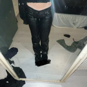 Svarta skinnbyxor - Säljer ett par svarta skinnbyxor som är supertrendiga och perfekta för en utekväll. De har en tight passform och är low waist, vilket ger en snygg siluett. Byxorna har fickor och en dragkedja framtill.