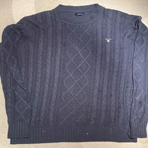Marinblå Stickad Gant tröja - En stickad, kabelmönstrad, tröja i bomull av märket GANT. Mycket bra skick. 