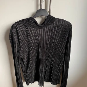 Svart topp - En svart topp från gina tricot med polo och lite öppen i ryggen. Materialet är lite glansigt och ribbat. 