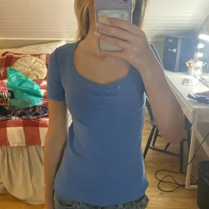 Blå ribbad topp - Säljer en snygg blå ribbad topp med korta ärmar och en fin rynkad detalj vid halsringningen. Perfekt för en avslappnad stil.