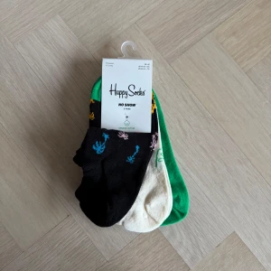 3-pack färgglada no-show strumpor från Happy Socks - Säljer ett set med färgglada no-show strumpor från Happy Socks. Setet innehåller strumpor i svart, grön och beige med roliga mönster. Perfekta för att ge en färgklick till din outfit utan att synas i skorna. Nypris 200 kr