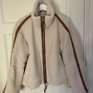 Beige teddyjacka från H&M - Mysig beige teddyjacka från H&M med bruna detaljer och dragkedja framtill. Jackan har en hög krage och är tillverkad av 100% återvunnen polyester. Perfekt för kyliga dagar🤗Vid frågor tveka inte på att höra av dig! Jackan är aldrig använd och är slutsåld på nätet och i butik.