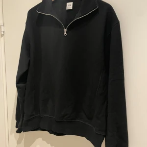 Svart tröja med dragkedja från Zara - Snygg svart tröja från Zara med halv dragkedja och hög krage. Perfekt för en avslappnad stil. Tröjan har långa ärmar och ribbade muddar vid ärmslut och nederkant.