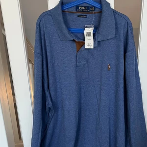 Blå pikétröja lång ärm  från Ralph Lauren  - Säljer en klassisk blå pikétröja från Ralph Lauren med lång ärm och den ikoniska loggan broderad på bröstet. Tröjan har en mjuk finish och en stilren krage. Perfekt för en avslappnad men stilfull look.