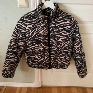 Zebramönstrad pufferjacka - Snygg zebramönstrad pufferjacka med dragkedja. Jackan har en hög krage och långa ärmar, perfekt för att sticka ut i mängden. Den är i en cool kombination av svart och rosa.