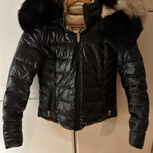 Svart / guldig jacka från Rockandblue - Unik limited edition jacka. Snygg figursydd jacka med avtagbar pälskrage. Jackan har två fickor med dragkedja. Knapparna är bak också så man kan justera hur tight det ska sitta runt midja. Man kan använda båda sidorna på jacka - svart eller guldig. Jackan är supervarm. Fyllningen är 80% dun och 20% fjädrar. Tyget är behandlat med BIONIC-FINISH® ECO.   Fått i present och aldrig använd- helt nytt och kvar papper på tofsar. Ha man stor byst så blir det mer som S 😊