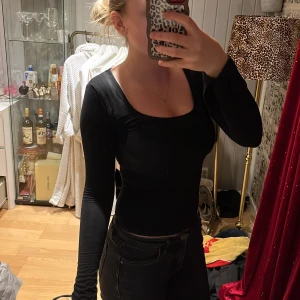 Svart långärmad topp - Säljer en stilren svart långärmad topp med en djup rund halsringning. Perfekt för en elegant och enkel look. Passar bra till både jeans och kjol.