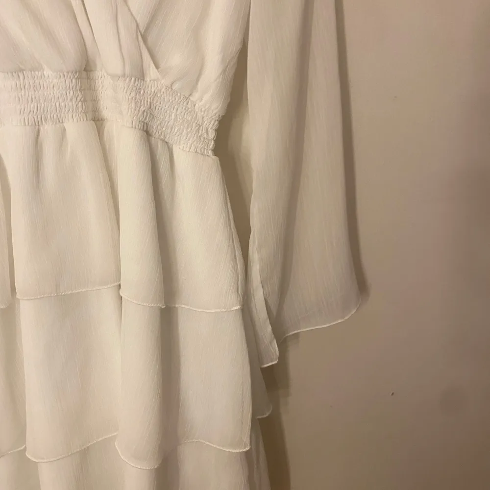 Elegant vit omlottklänning från Bubbleroom med långa ärmar och smockdetaljer i midjan. Klänningen har en v-ringad design och ett flödande tyg som ger en luftig känsla. Endast använd 1 gång. . Mekot.