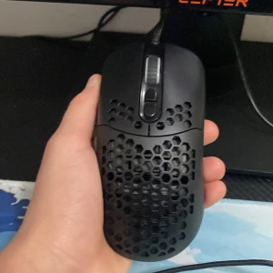 Svart gamingmus med RGB-belysning - Säljer en svart gamingmus med en lätt och ergonomisk design. Musen har en perforerad yta med hexagonmönster för bättre grepp och ventilation. Den är utrustad med RGB-belysning som lyser i blått. Perfekt för långa spelsessioner.