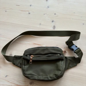 Olivgrön magväska med dragkedjor - Säljer en praktisk olivgrön magväska från Oitibao. Väskan har flera fack med dragkedjor och en justerbar rem för bekväm passform. Perfekt för att hålla dina saker säkra och lättillgängliga.