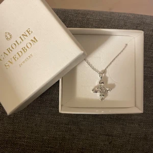 Halsband med kristallkors/stjärna från Caroline Svedbom - Elegant halsband från Caroline Svedbom med ett gnistrande kristallkors i silverfärg som också kan ses som en stjärna. Helt oanvänt och fortfarande orört. Kommer i originalförpackning. Pris kan diskuteras vid snabb affär💞💞