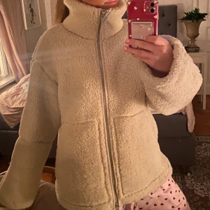 Beige teddyjacka med högkrage - Mysig beige teddyjacka med hög krage och dragkedja framtill. Jackan har används innan så bild 2. 
