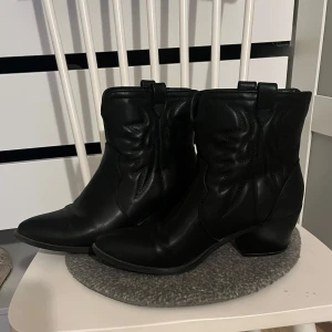 Svarta cowboy boots - Snygga svarta cowboy boots i skinn med spetsig tå och dekorativa sömmar. Perfekta för en stilren look med en touch av vilda västern. De har en bekväm klack som ger lite extra höjd.