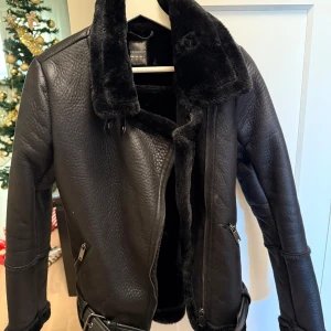 Svart skinnjacka med fuskpäls - Snygg svart skinnjacka från Primark med mjuk fuskpäls på insidan och kragen. Jackan har dragkedja och bälte i midjan. Perfekt för kyliga dagar.