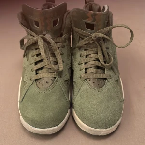 Gröna Nike Air jorden sneakers basket skor   - Snygga gröna Nike Air sneakers med orange detaljer och snörning. Skorna har en unik design med en kombination av mocka och syntetmaterial. Perfekta för en sportig look.