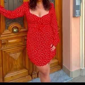 Adoore  - Charmig röd klänning med vita blommor och snörning framtill från Adoore❤️ Den har långa ärmar och en kort längd. Storlek 44, lite stretch. 