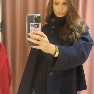Blå kappa med hög krage - Snygg blå kappa med hög krage och knappar framtill. Perfekt för kyligare dagar och ger en stilren look. Passar bra till både jeans och klänning. Köptes på Gina, prislappen finns kvar och har inte använt då den inte passa mig så bra när jag är lång! 