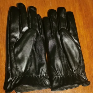 Svarta skinnhandskar med knäppning - Snygga svarta skinnhandskar med stilren design och praktisk knäppning vid handleden. Perfekta för kyliga dagar med mjukt foder för extra värme. Passar både till vardags och mer uppklädda tillfällen.