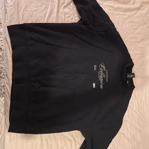Svart sweatshirt från Collusion - Säljer en svart sweatshirt från Collusion med tryck framtill. Tröjan har långa ärmar och en rund halsringning. Perfekt för en avslappnad stil.
