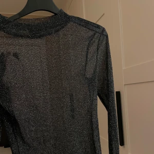 Svart glittrig topp från Gina Tricot - Snygg svart glittrig topp från Gina Tricot i storlek XS. Toppen har en transparent look med långa ärmar och en tight passform, perfekt för en festlig kväll. Endast använd 2 gånger!
