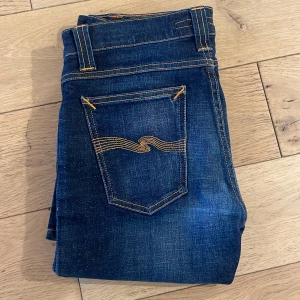 Mörkblå jeansbyxor - Feta mörkblåa Nudie jeans i modellen Tube Tom. Använt men riktigt bra skick utan några defekter. Storlek W30 L32. Pris kan diskuteras, nypris 1800. Skriv gärna vid minsta fundering!