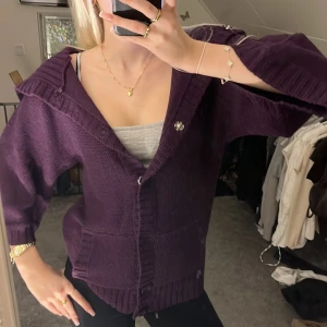 Lila stickad kofta med knappar - Säljer en mysig lila stickad kofta med stora knappar och trekvartsärmar. Koftan har en avslappnad passform och ribbade detaljer vid ärmslut och nederkant.Lite stor för mig som har XS