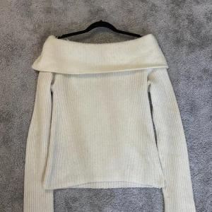Vit stickad offshoulder-tröja - Säljer en beige vit stickad offshoulder-tröja med långa ärmar. Perfekt för kyligare dagar och ger en elegant touch till din outfit. Tröjan har en ribbad struktur som ger extra komfort och stil.