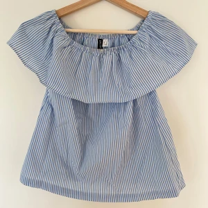 Blå- och vitrandig offshoulder topp från Divided - Snygg blå- och vitrandig offshoulder topp. Perfekt för vår och sommar!  Luftig design och elastiska halslinning, volangdetalj. Väldigt fint skick! Liten fläck på insidan av kragen (se bild).