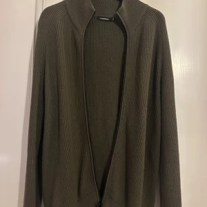Olivgrön ribbad kofta från J.Lindeberg - Snygg olivgrön kofta från J.Lindeberg i ribbat material. Perfekt för lager-på-lager under kyliga dagar. Koftan har en stilren design med dragkedja framtill. Strl S men passar 