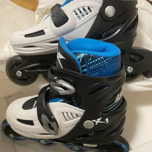 Svart och vit inlines från Atlanta - Säljer ett par coola inlines från Atlanta i svart och vit med blå detaljer. De har justerbar storlek mellan 35-38 och är utrustade med spännen för säker passform. Perfekta för en rolig åktur!